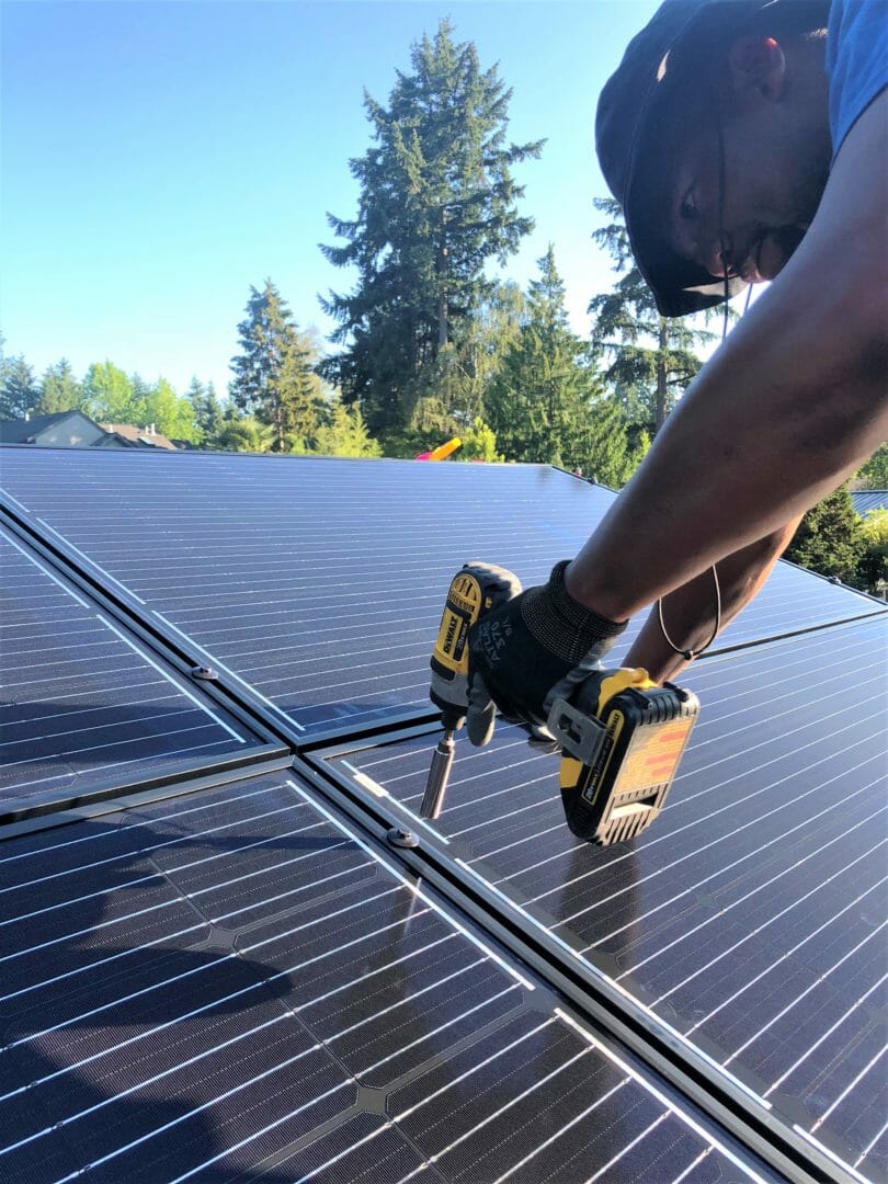A Sphere Solar Energy crew members bolt a panel in place on the metal rooftop of a Mercer Island home.